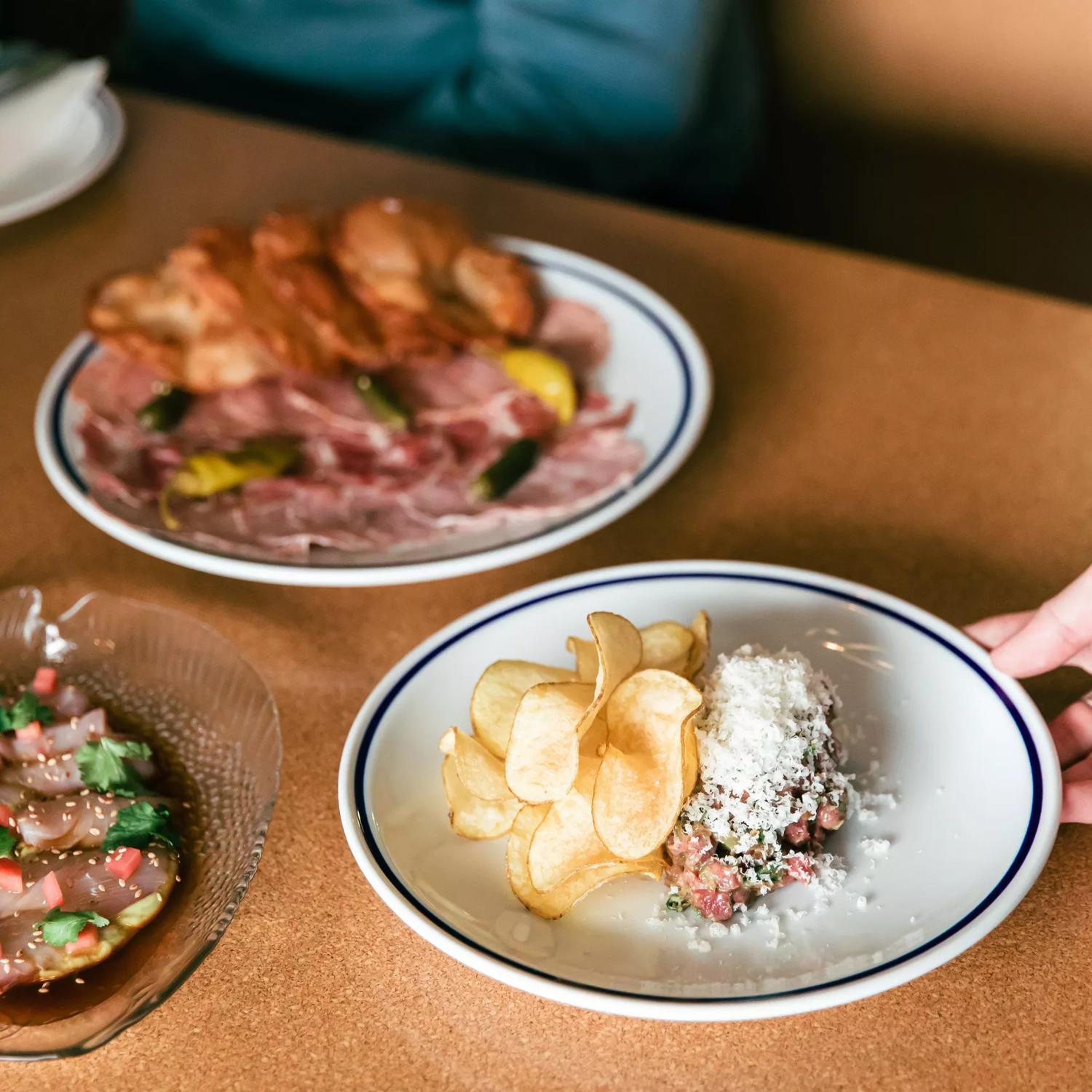 A hand holding a dish inside Margot, with 2 other dishes already on the table.