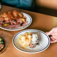 A hand holding a dish inside Margot, with 2 other dishes already on the table.