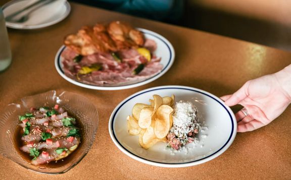 A hand holding a dish inside Margot, with 2 other dishes already on the table.
