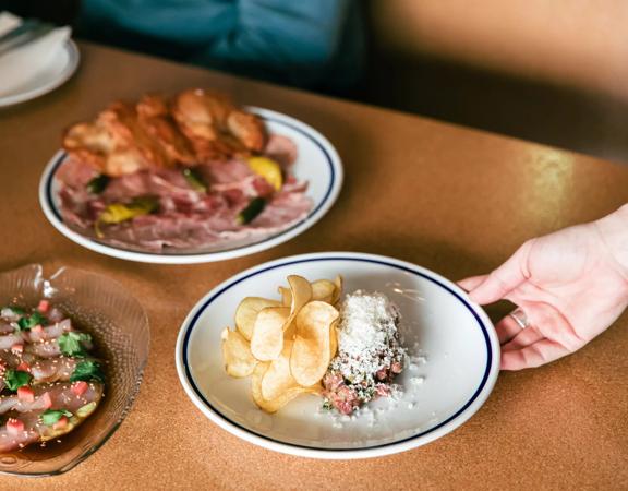A hand holding a dish inside Margot, with 2 other dishes already on the table.