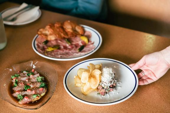 A hand holding a dish inside Margot, with 2 other dishes already on the table.