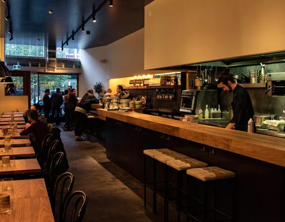 The dim and moody interior of Highwater eatery with customers siitng and bar staff working.