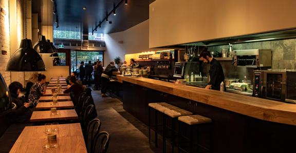 The dim and moody interior of Highwater eatery with customers siitng and bar staff working.