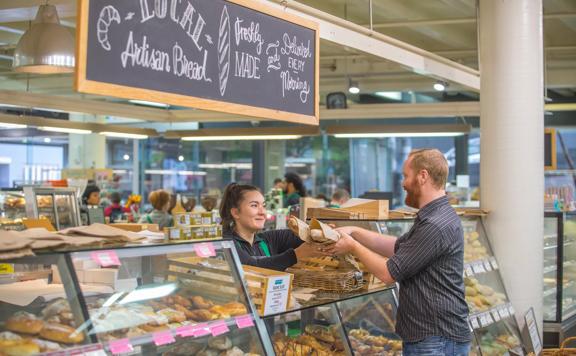 Staff member handing over a brown paper bag full of bread to a customer inside Moore Wilsons.