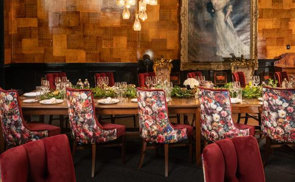 Five floral chairs sit at a long table inside a room of QT Wellington.