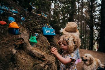 Two kids and a god look at smurf houses in the forest.