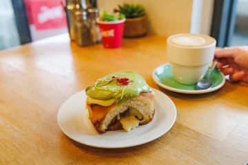 A pistachio cream-topped cinnamon scroll on a plate beside a coffee at Urban Eatery in Tawa.