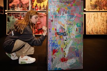 Child writing on a graffiti covered pole with a marker pen.