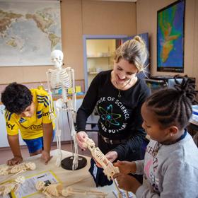 2 Young children and an adult inspect mini plastic skeletons at house of Science.