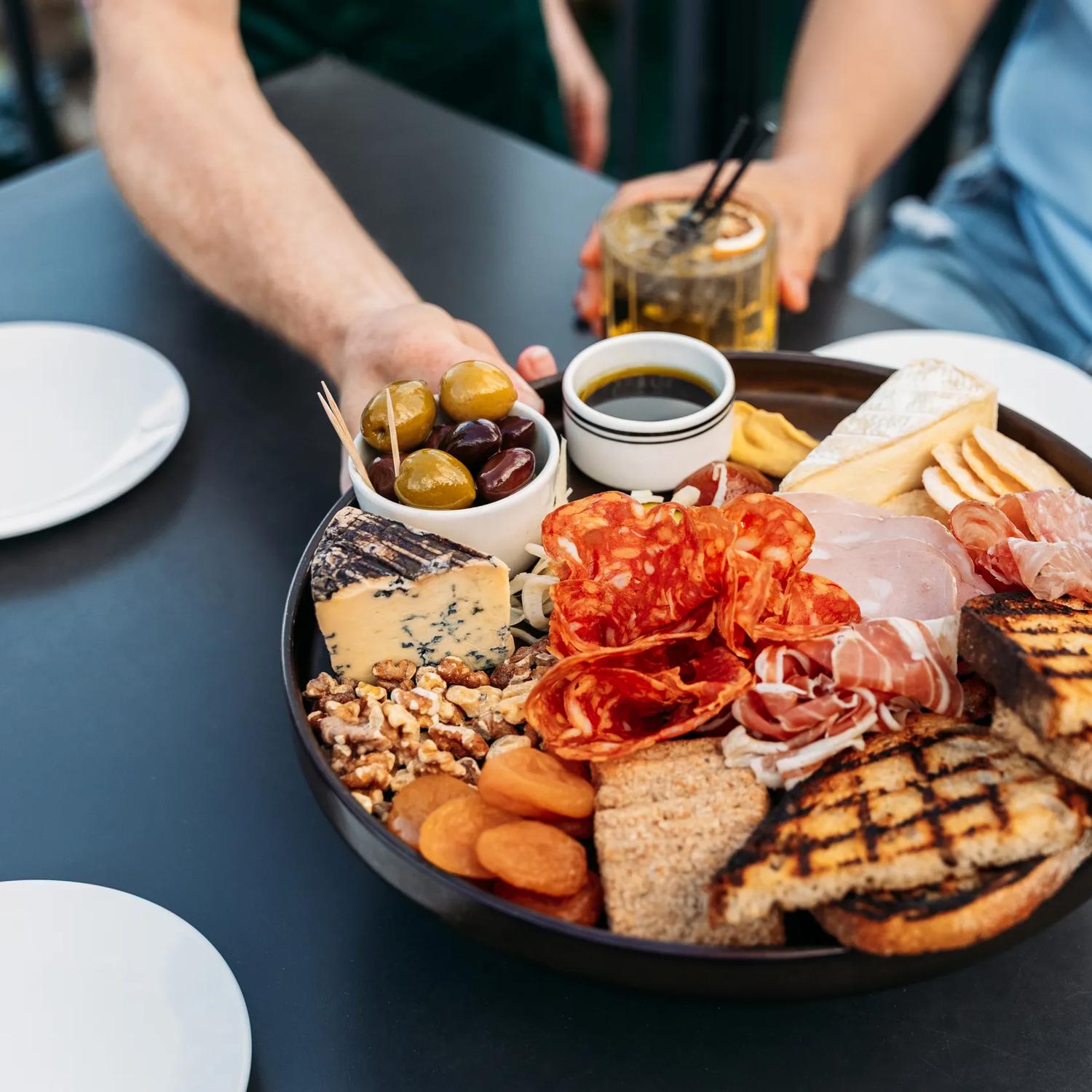 Three people grabbing food from a charcuterie board at Foxglove on Queens Wharf.