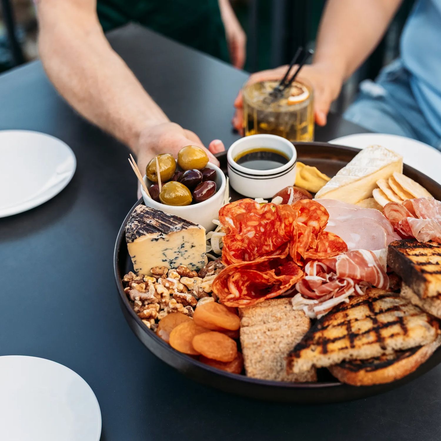 Three people grabbing food from a charcuterie board at Foxglove on Queens Wharf.