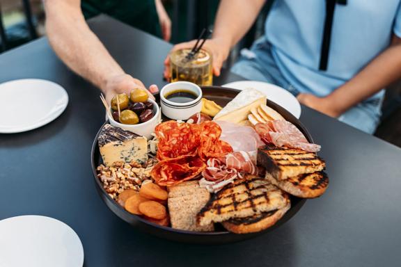 Three people grabbing food from a charcuterie board at Foxglove on Queens Wharf.