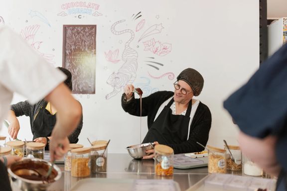 A person making chocolate at Wellington Chocolate Factory on the Chocolatier expereince. They are lifting a spatula from a bowl with chocolate dripping from it.