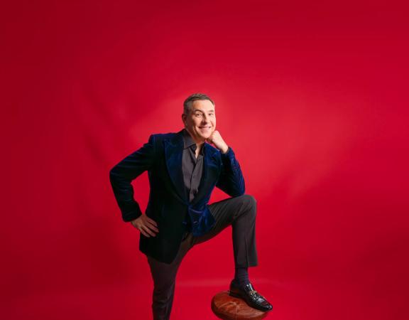 British comic, David Walliams, posing in front of a red wall to promote his upcoming show in Wellington’s St James Theatre. 