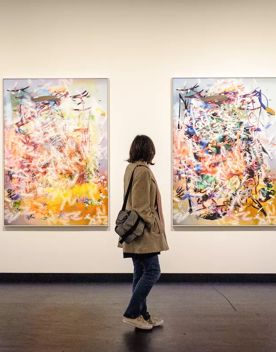 A person standing between and facing 2 art installations, depicting abstract colourful lines.
