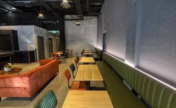 The café at Microtel by Wyndham Wellington, a four-star hotel located on Vivian Street in Te Aro, Wellington. The walls are grey, the seating is dark green and orange and tables are light-coloured wood.