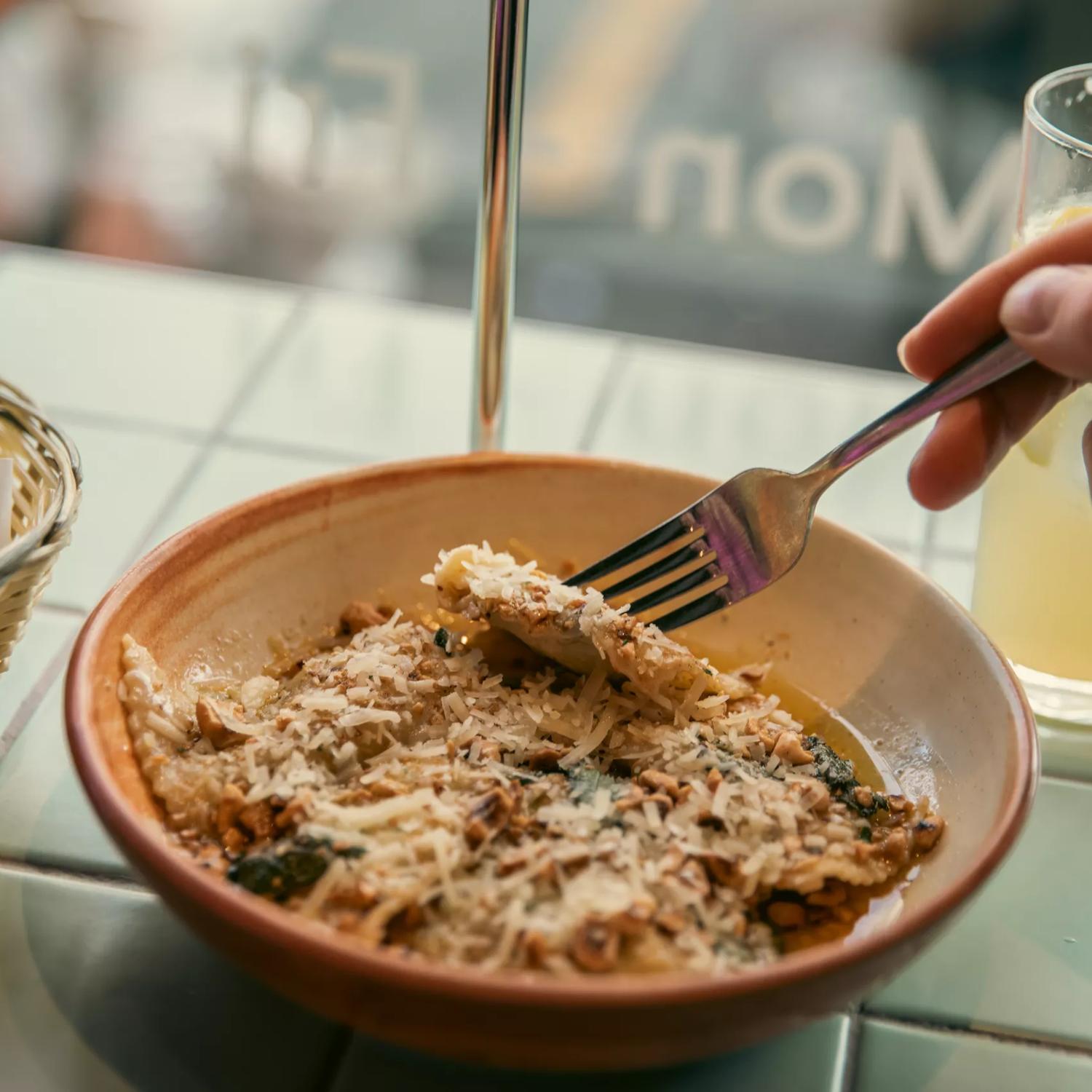 Close-up of a hand holding a fork and digging into a bowl of ravioli at 1154 Pastaria on Cuba Street.