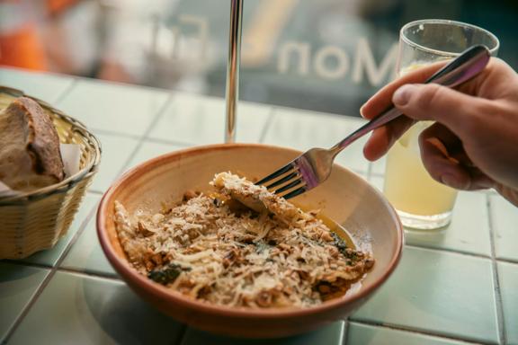 Close-up of a hand holding a fork and digging into a bowl of ravioli at 1154 Pastaria on Cuba Street.