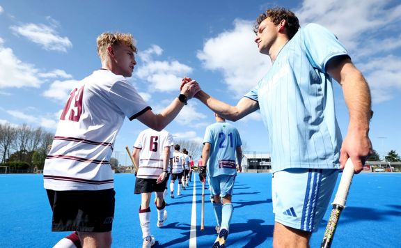 Opposing field hockey players shake hands.