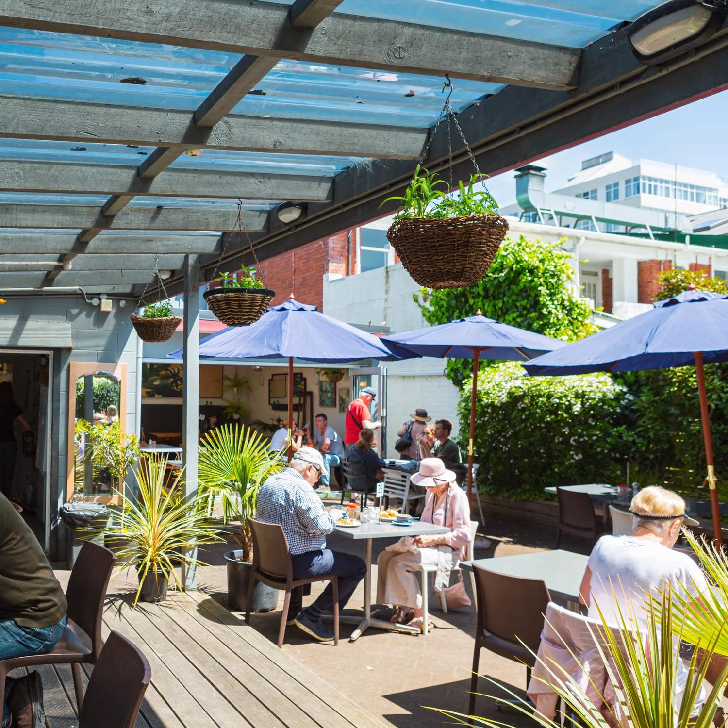 People sit at tables on the sun-soaked deck at Hive. Blue sun umbrellas provide shade.