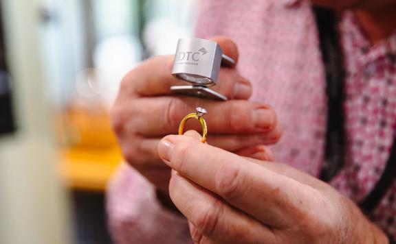 Close up of a person’s hands holding a diamond ring looking through a magnifying glass.