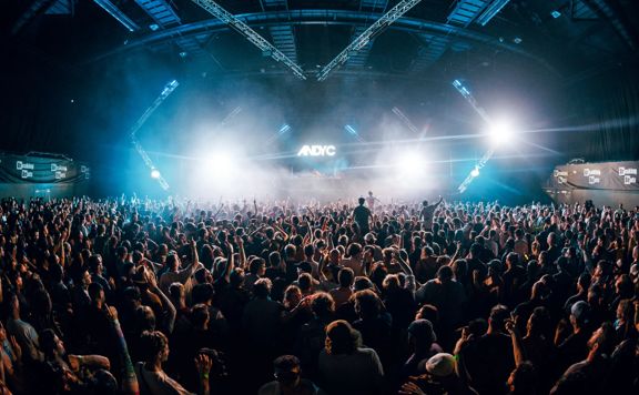 An electronic music concert at TSB Arena with a packed audience.