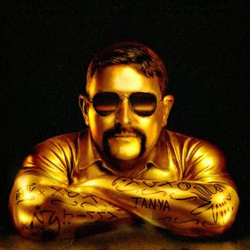 Gold-toned portrait of a Heath Franklin Chopper wearing aviator sunglasses and a collared shirt, resting crossed arms covered with tattoo-like markings against a dark background.