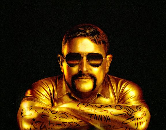 Gold-toned portrait of a Heath Franklin Chopper wearing aviator sunglasses and a collared shirt, resting crossed arms covered with tattoo-like markings against a dark background.