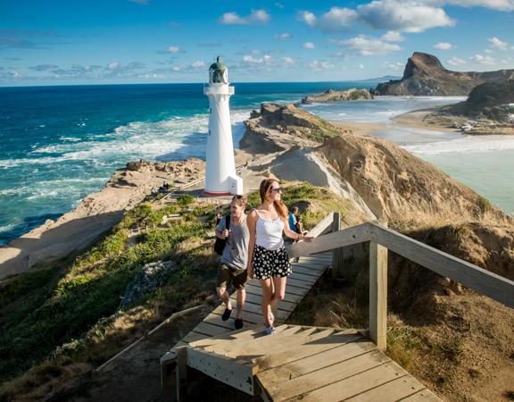 Two people are walking up the steps in front of the Castlepoint Lighthouse in the Wairarapa region.