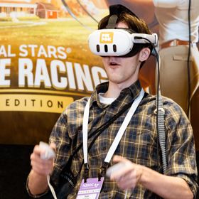 A delegate at the New Zealand Game Developers Conference 2024 wears a VR headset and holds two controllers, playing a game.