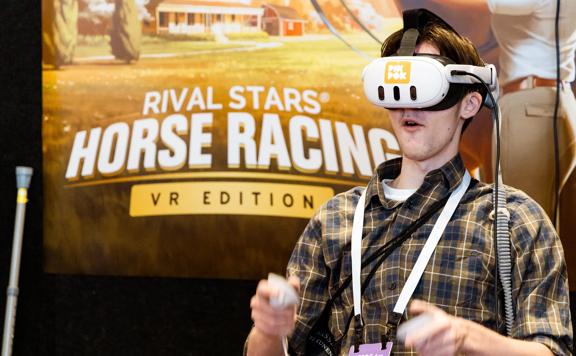 A delegate at the New Zealand Game Developers Conference 2024 wears a VR headset and holds two controllers, playing a game.