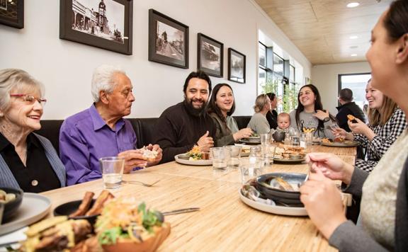 A whānau (family) sat at a table inside Kāinga eatery, enjoying their meals and chatting.