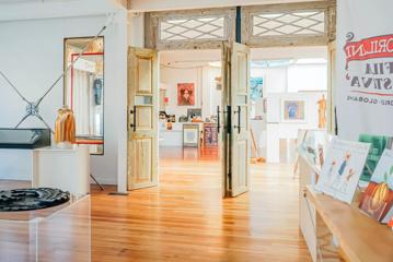 Inside a bright room with white walls, hardwood floors and wooden double doors leading to a gallery space.