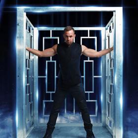 Illusionist Anthony Street stands with outstretched arms inside a metal frame on  a stage.