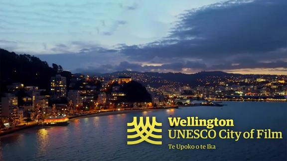 Looking across the water towards Oriental bay and the Wellington water front at sunset. Wellington UNESCO City of Film Te Upoko o te Ika is written on the image with yellow font.