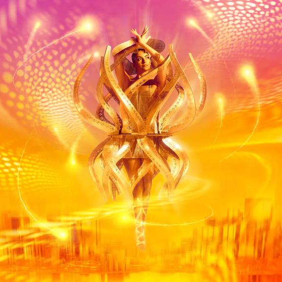 A person wears The Golden Chakra design from World of WearableArt. The background is a mix of purple, yellow, and orange graphics.