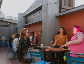 Three friends are laughing over a drink at Ascot's rooftop patio.