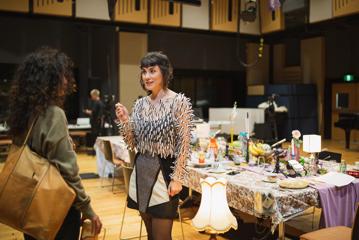 Two people stand and chat at a large table filled with eclectic items on the right.