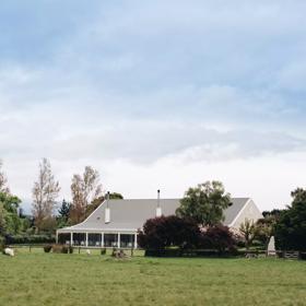 Venue building in centre of picture, surrounded by green and purple trees, with paddocks and sheep in the foreground.