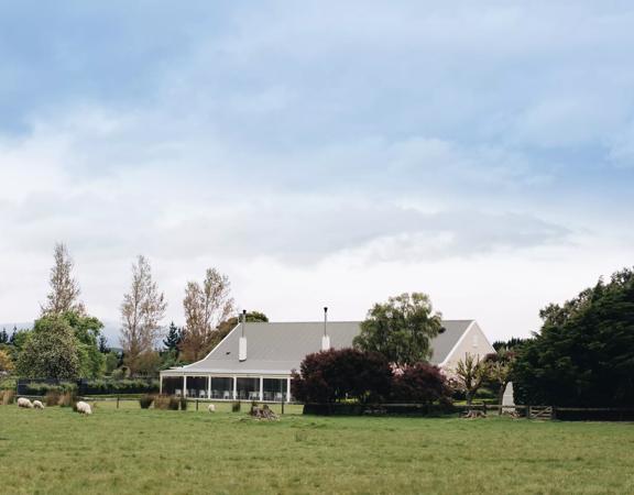 Venue building in centre of picture, surrounded by green and purple trees, with paddocks and sheep in the foreground.