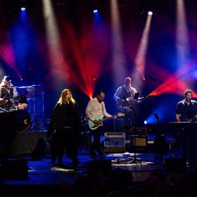 The Fleetwood Mac Experience, a tribute band, performs on stage with blue and red lights. 