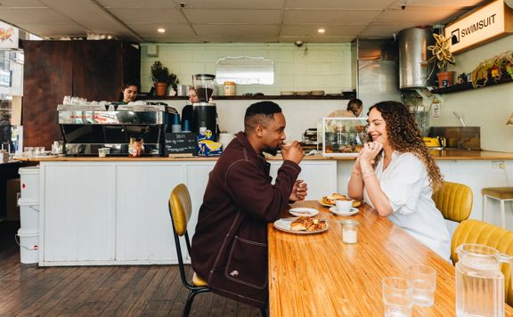 Two people sharing coffee and a meal inside Swimsuit on Dixon Street. The coffee counter is behind them with baristas working.