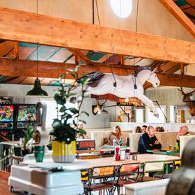 The interior of Seashor Cabaret, a diner located on The Esplanade and Sidney Street in Petone, with four vintage arcade games, two taxidermy deer heads on the wall, two large tables with eight chairs each and three wood booths with eight customers seated.