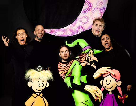 Five cast members of 'Badjelly the Witch Glow Show' wear all black and pose for a photo with the puppet characters from the show.