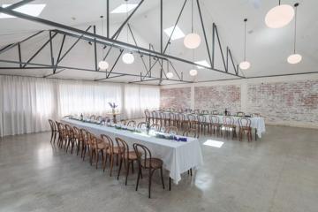 The interior of Whisky and Wood, an event venue in Wellington Central, setup with two long banquet tables, with white table clothes and twenty wooden chairs at each, exposed brick walls and circular lights suspended from the ceiling.