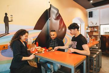 Two people sit at a high-top table as a waiter delivers the two burgers they ordered to the table.