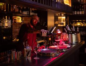 A bartender pours a glass of red wine in a dark cozy wine bar.