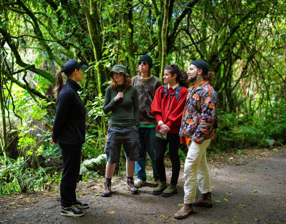 A Zealandia staff member leads a group of four friends on a walking tour in the forest.