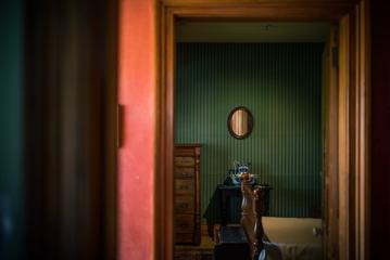 A dark bedroom inside the Nairn Street Cottage in Wellington. There is a small oval mirror affixed to the pin-striped wall, a wood dresser and a bed.