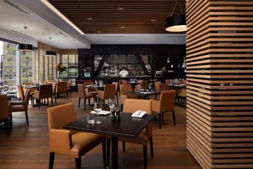 A modern restaurant with square tables, leather chairs, wood, and black decor.